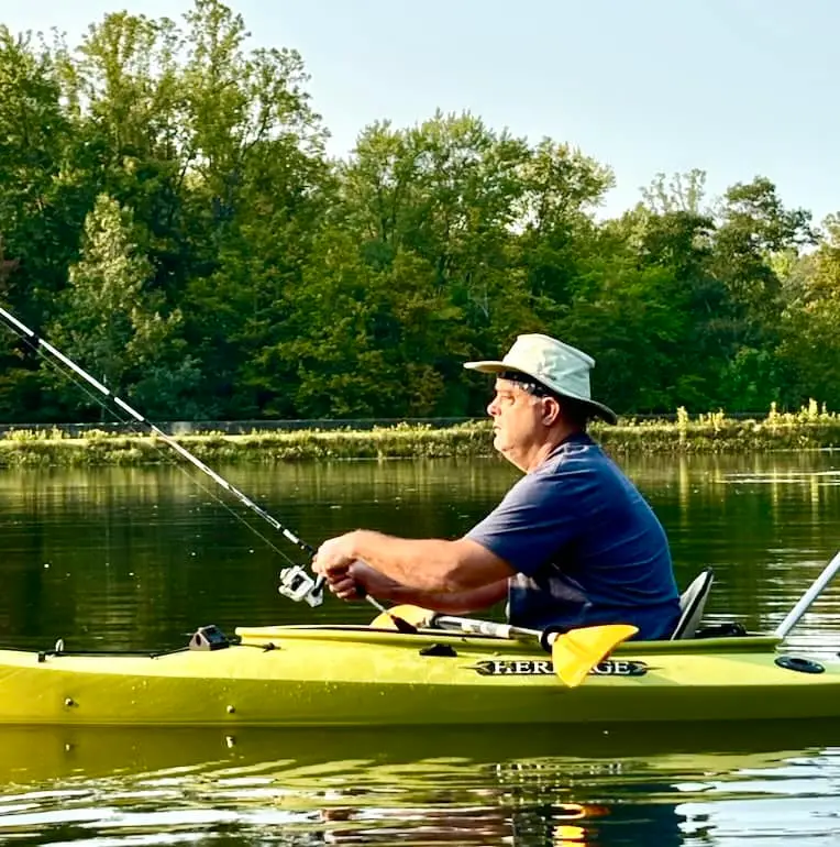 A man fishing from a kayak on a calm stretch of water